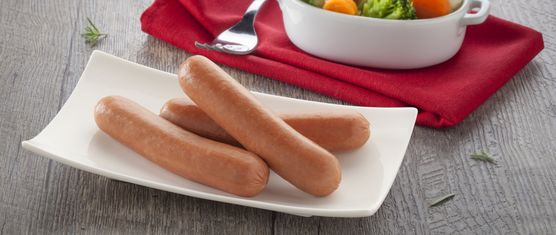 Three Doux Chicken Franks on a white plate with a side of small vegetables in a small white container